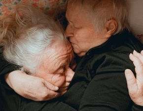 Twee oudere mensen knuffelen warm en liefdevol, een mooie herinnering aan genegenheid in de comfort van huis of zorgomgeving.