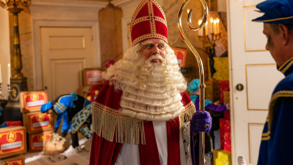 Santa Claus in een feestelijke setting met cadeaus en versieringen bij Cinema Middelburg.
