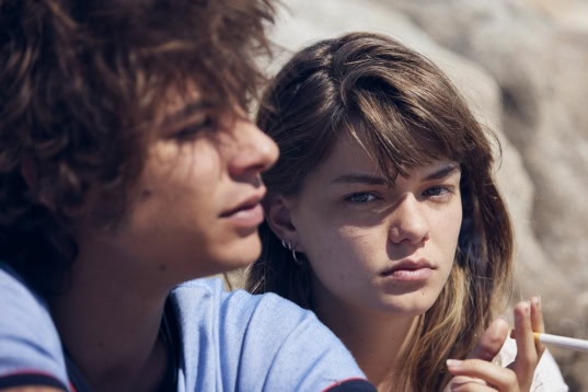 Alt tekst: Twee jongvolwassenen zitten dicht bij elkaar in een bioscoop, kijken naar het scherm met geconcentreerde blikken, metal en een relaxte sfeer.