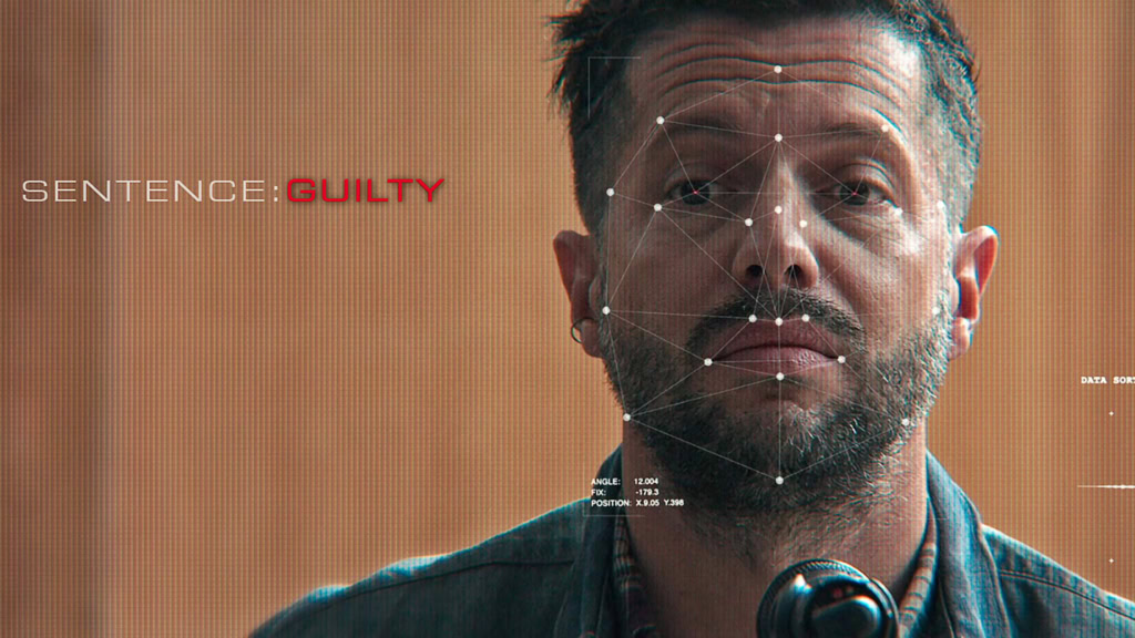 Filmstill uit "Artificial Justice" met een man met een baard en korte haar, die een serious blik heeft, geschikt voor een filmtheater website over belangrijke films.