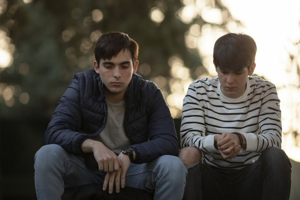 Twee jonge mannen zitten samen buiten, verdiept in gedachten, met een rustige bosachtergrond. Perfect voor een film over integriteit en vriendschap, passend bij de film 'Hombres Integros' en de sfeer.