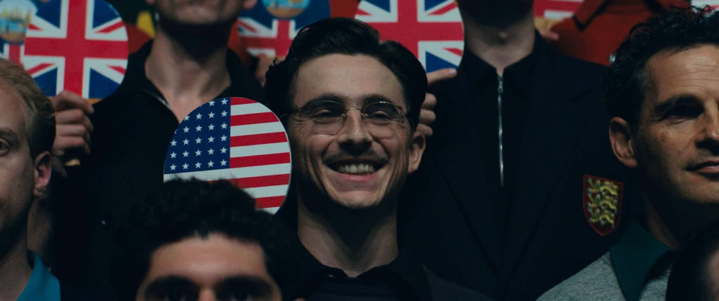 Marty Supreme, lachend man met Amerikaanse vlag op achtergrond, in een filmtheater setting bij Cinema Middelburg, perfect voor film- en entertainmentliefhebbers.