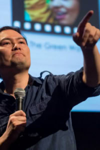 Een spreker tijdens een filmcollege presentatie in Cinema Middelburg, met een microfoon in de hand en een scherm met filmbeelden op de achtergrond.