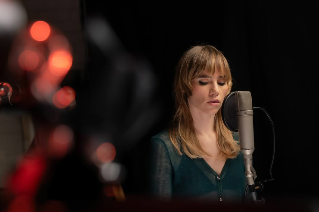 Zij staat voor een microfoon in een geluidsstudio, klaar om te zingen of op te nemen, met een geconcentreerde uitdrukking. De achtergrond is donker en de scène straalt professionaliteit uit, perfect v.