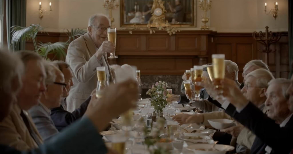 Ouderen genieten samen van een feestelijk diner in een klassieke, elegante eetzaal met houten panelen en kroonluchters, terwijl ze toosten met glazen champagne.