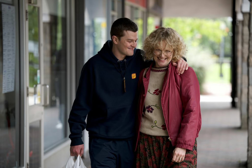 Een jonge man en een oudere vrouw lopen samen door de lobby van Cinema Middelburg, lachend en genietend van elkaars gezelschap, wat een warme en vriendelijke sfeer uitstraalt.
