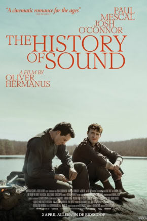 Filmstill uit "The History of Sound" met twee mannen zittend op een houten pier bij een meer, onder een heldere hemel, met een rustige natuurlijke achtergrond.