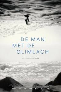 Man die op het strand ligt ondersteboven, met de zee en golven op de achtergrond, in zwart-wit.