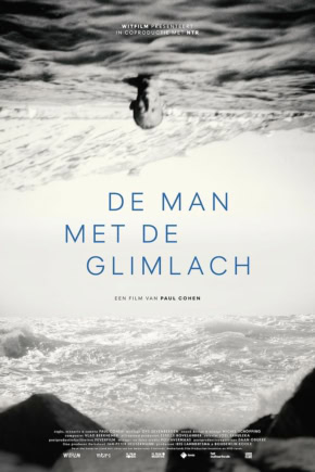 Man die op het strand ligt ondersteboven, met de zee en golven op de achtergrond, in zwart-wit.