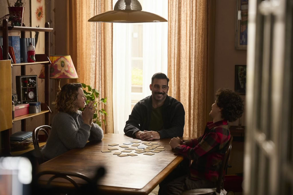 Gezinsmoment in woonkamer met ouders en kinderen die samen een bordspel spelen, ontspannen en genieten van quality time in een gezellige, huiselijke sfeer.