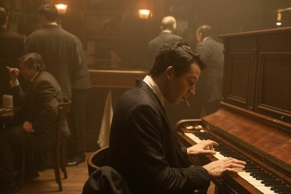 Een man speelt piano in een vintage theater, omringd door mensen die genieten van een live muziekoptreden, passend bij het thema 'De Geschiedenis van Geluid' en de sfeer van een klassieke filmzaal.