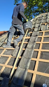 Man voert duurzaam dakonderhoud uit op een woning met traditionele dakpannen, met aandacht voor milieuvriendelijke technieken en materialen.