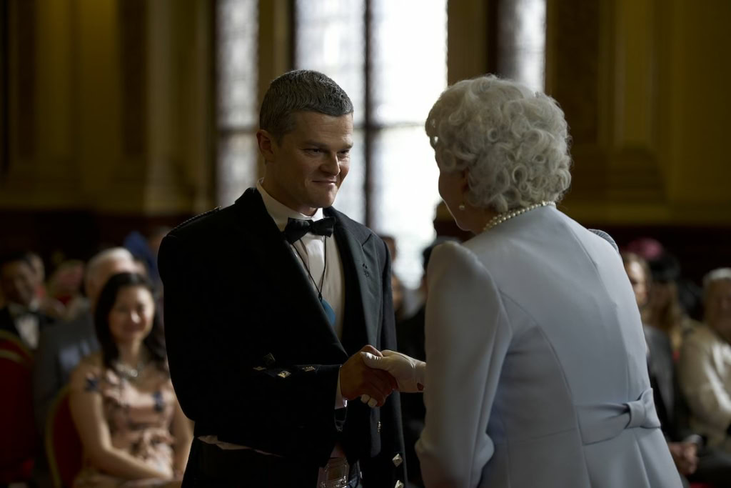 Jongetje in pak geeft hand aan oudere vrouw tijdens een ceremonie in een filmtheater, met een publiek op de achtergrond, passend bij een cinema-omgeving.