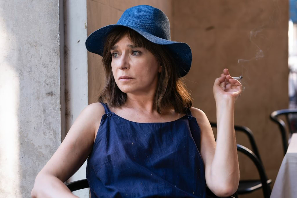 Vrouw in blauwe jurk en hoed die binnen in een filmtheater zit, genietend van een film, met een sigaret in haar hand, in een gezellige en comfortabele omgeving bij Cinema Middelburg.