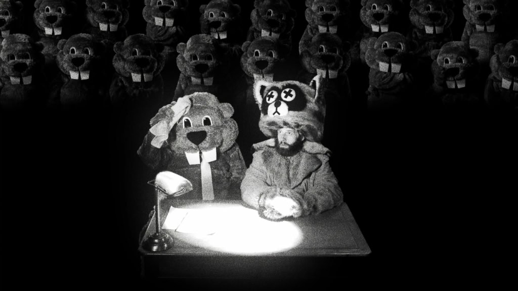 Een zwart-wit afbeelding van mascottes en poppen in een filmzaal, met een mascotte die aan een bureau zit en een andere mascotte die een hand op haar hoofd heeft, symboliserend entertainment en filmer.