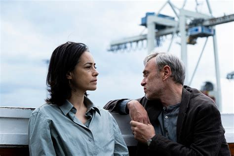 Twee mensen hebben een intens gesprek op de kade met een haven en kraan op de achtergrond, mogelijk voor een film of theaterproductie in Middelburg.