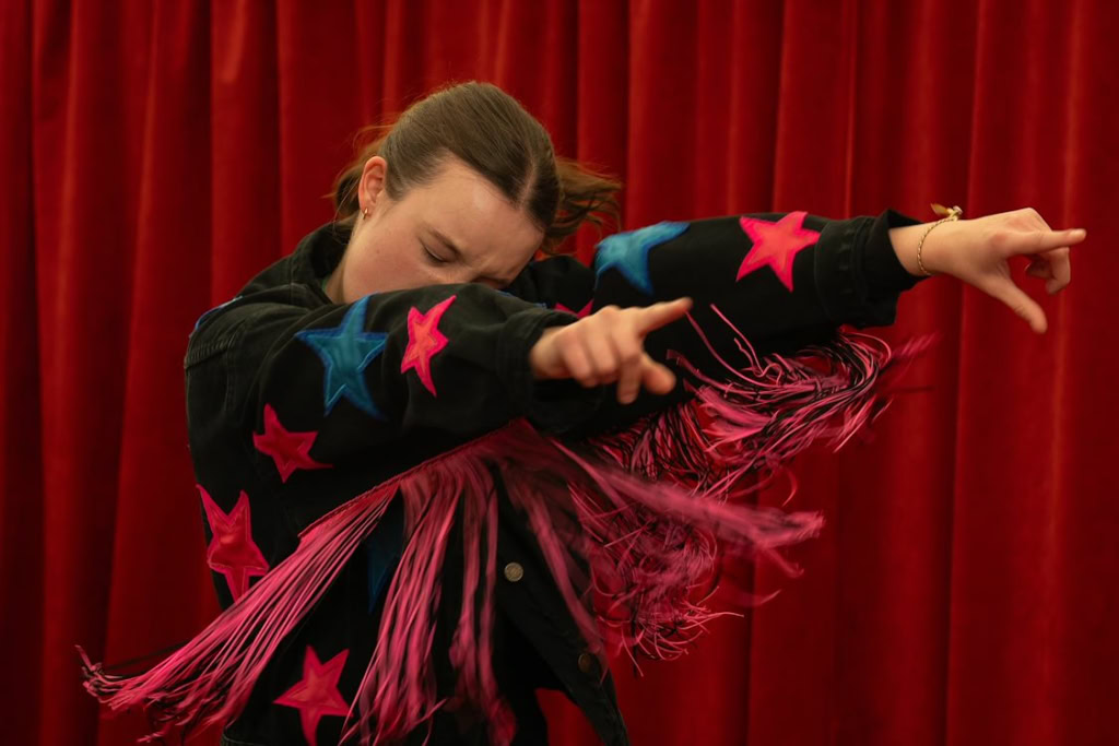Dansvoorstelling met jonge danseres die expressief beweegt voor een rode theaterachtergrond.