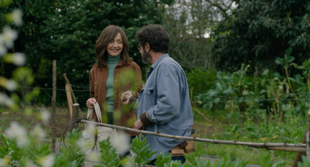 Tuinieren in de tuin van een filmtheater, met twee mensen die praten en lachen, omgeven door groene planten en bomen, in een ontspannen sfeer.