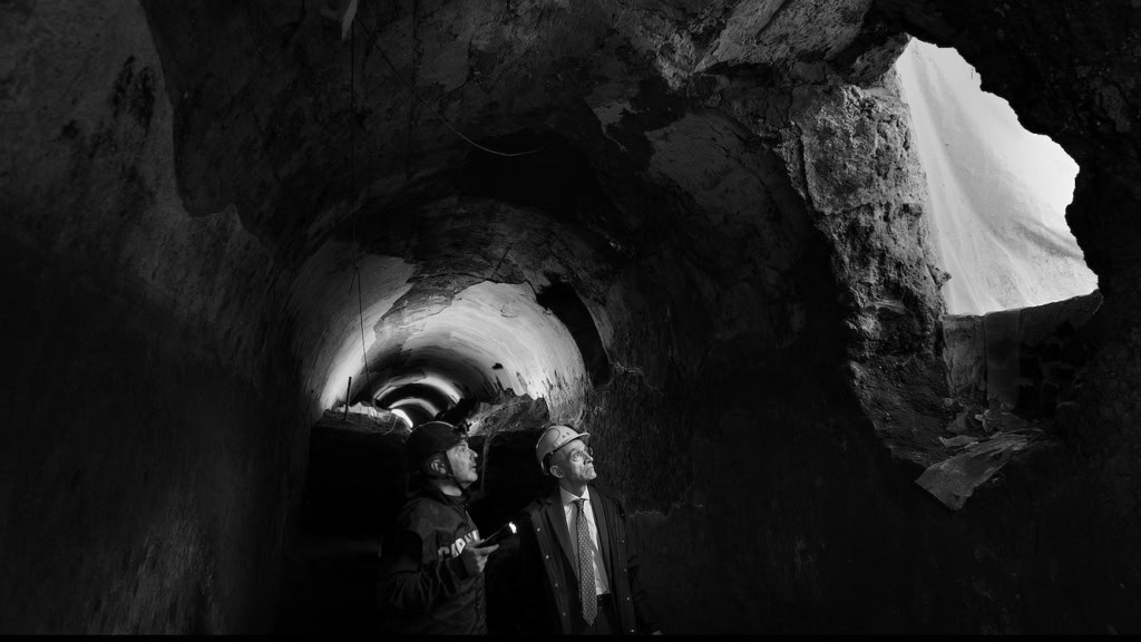 Twee mensen bekijken de ondergrondse tunnel bij Cinema Middelburg, met een indrukwekkende rotswand en een lichtinval die door de opening schijnt.