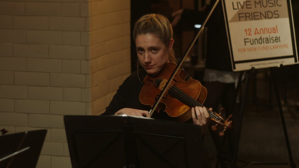 Muzikant speelt viool tijdens een live optreden in een theater, met een poster op de achtergrond voor een benefietconcert.