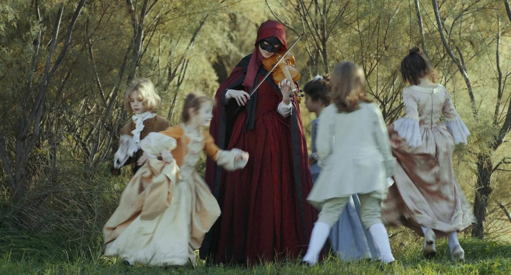 Historische kostuumfeest met kinderen en een vrouw in een rood kostuum in een bosrijke omgeving.