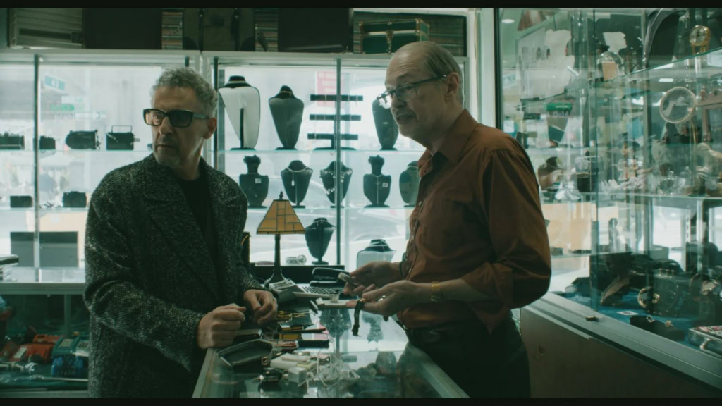 Twee mannen die een antiekwinkel bezoeken, bekijken sieraden en oude voorwerpen in een glazen displaykast.