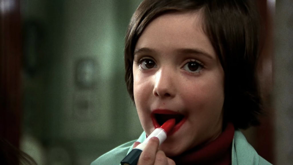 Meisje met kort bruin haar en rood lippenstift, die een lippenstift aanbrengt, in een filmachtige scène.