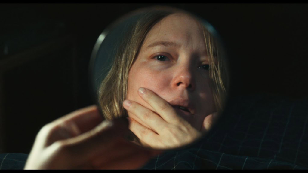 Close-up van een vrouw die in een spiegel kijkt met een bezorgde uitdrukking, benadrukt emotie en spanning in de film L'Inconnue.