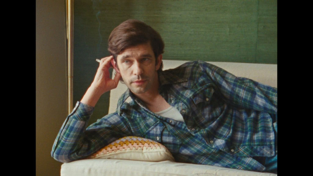Portret van een man liggend op een bed, met een hand onder zijn hoofd, in een casual setting, met groene muur op de achtergrond.