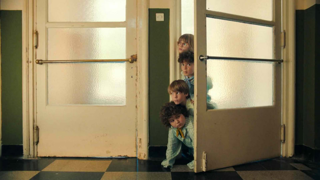 Drie kinderen verstoppen zich achter openstaande deur in een school of theater, nieuwsgierig en speels, met een vintage uitstraling.