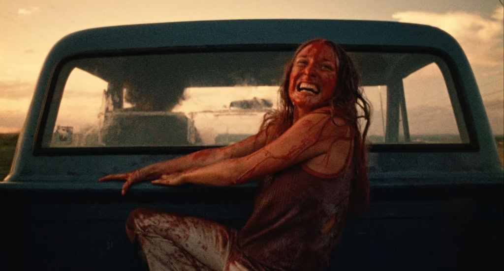 Vrouw met bloed op haar gezicht en kleding, lachend terwijl ze op een auto zit, scène uit de horrorfilm 'The Texas Chain Saw Massacre' ter viering van de 50e verjaardag.