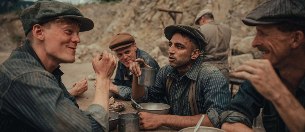 Mannen in vintage kleding zitten samen in een natuurlijke omgeving, genieten van een maaltijd en gesprekken voeren, sfeer van historische film.
